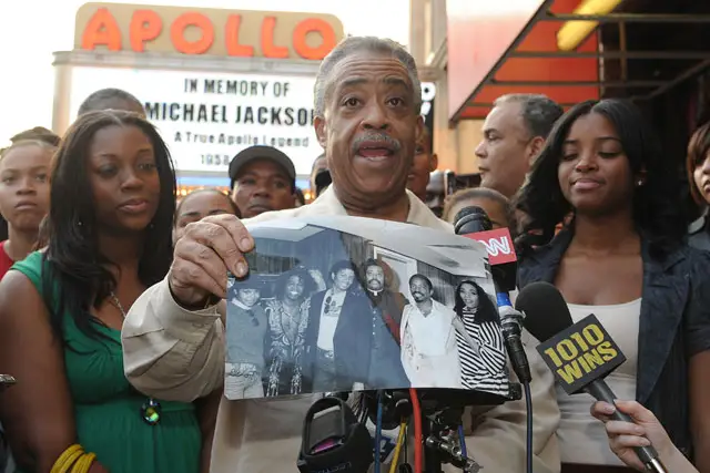 Rev. Al Sharpton holds a black and white photograph of himself and Michael Jackson outside the Apollo Theatre.